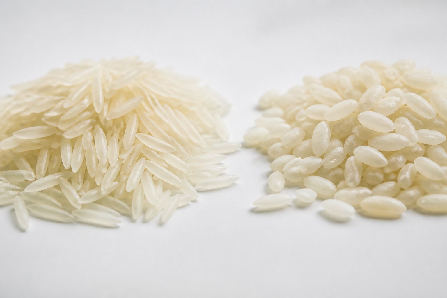 Close-up of two piles of rice grains, one with long slender basmati rice and the other with larger super kernel rice, on a plain surface.