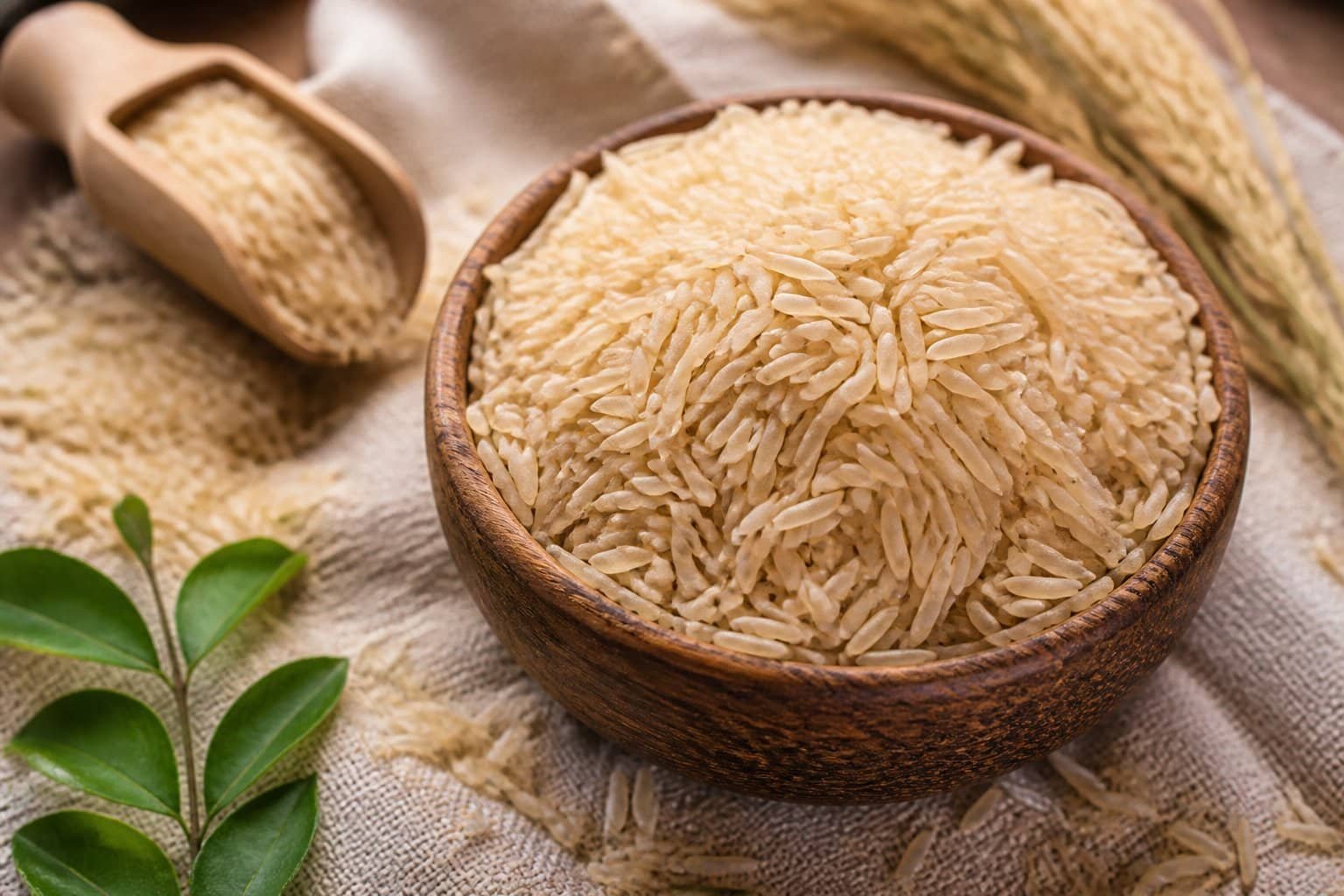 Close-up of uncooked brown basmati rice grains in a wooden bowl with some grains scattered around on a cloth.